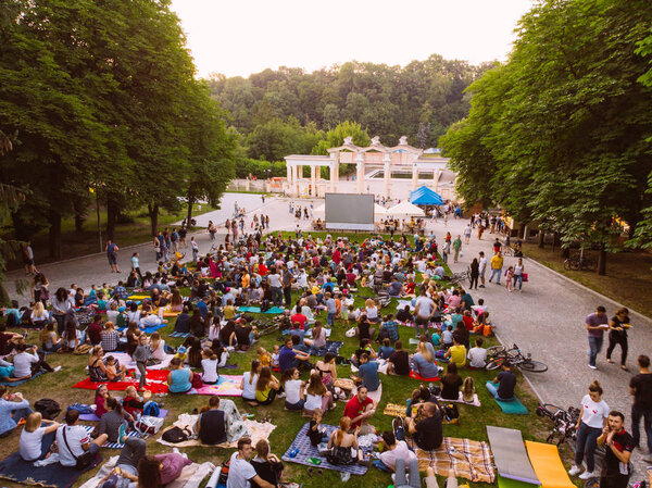 LVIV, UKRAINE - JUNE 1, 2018: people sitting on grass in city park watching movie in open air cinema