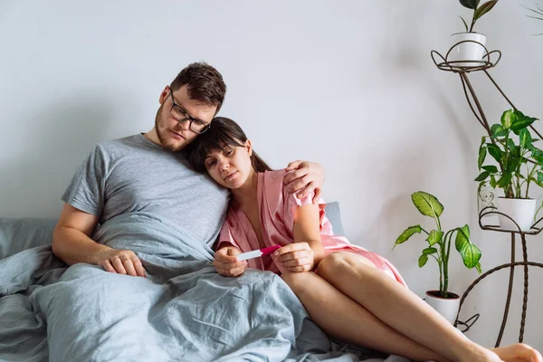 sad couple in bed looking at negative pregnancy test