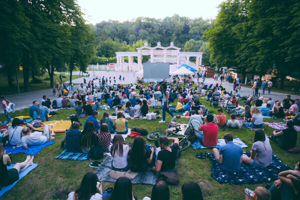 LVIV, UKRAINE - JUNE 1, 2018: people sitting on grass in city park watching movie in open air cinema