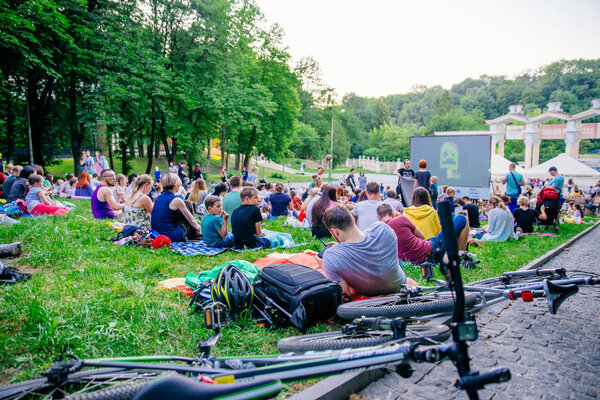 LVIV, UKRAINE - JUNE 1, 2018: people sitting on grass in city park watching movie in open air cinema