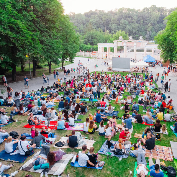 LVIV, UKRAINE - JUNE 1, 2018: people sitting on grass in city park watching movie in open air cinema