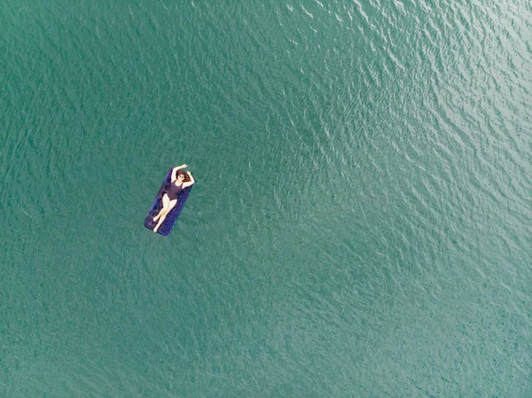 woman on mattress in azure water. overhead view. copy space. summer time