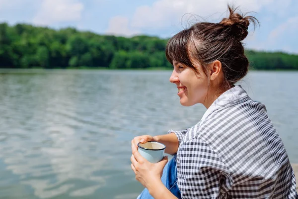 坐在木码头上的年轻成年女子喝咖啡看湖 — 图库照片