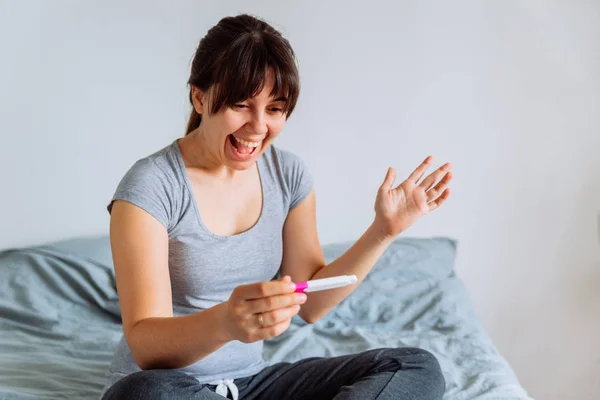 Unga Lyckliga Kvinnan Sitter Sängen Tittar Positivt Graviditetstest — Stockfoto