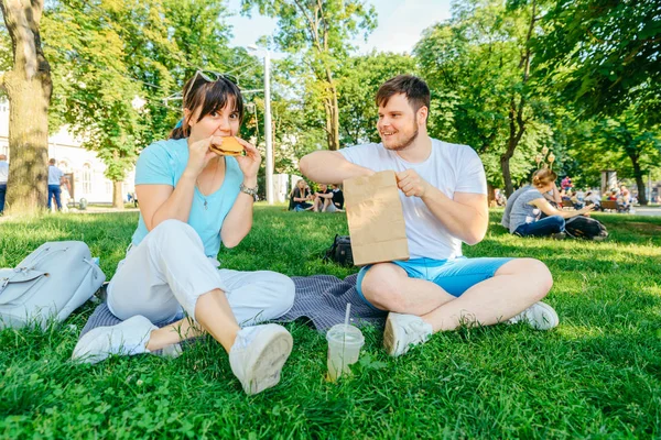 Çift yüzlü içme hamburger yeme yeşil çimenlerin üzerinde oturuyor. geniş melek