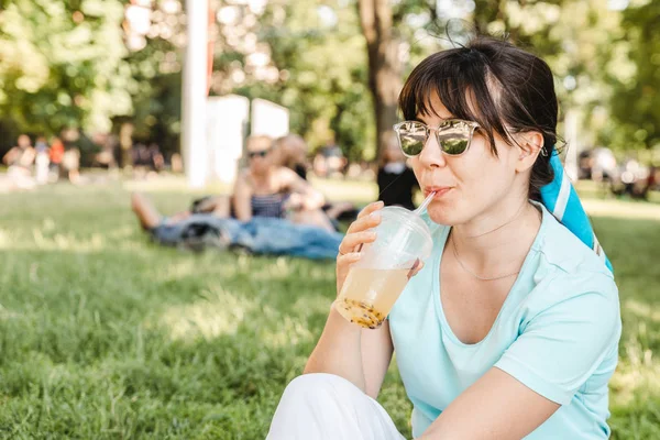 woman holding cool drink in city park. blurred background. wide angel