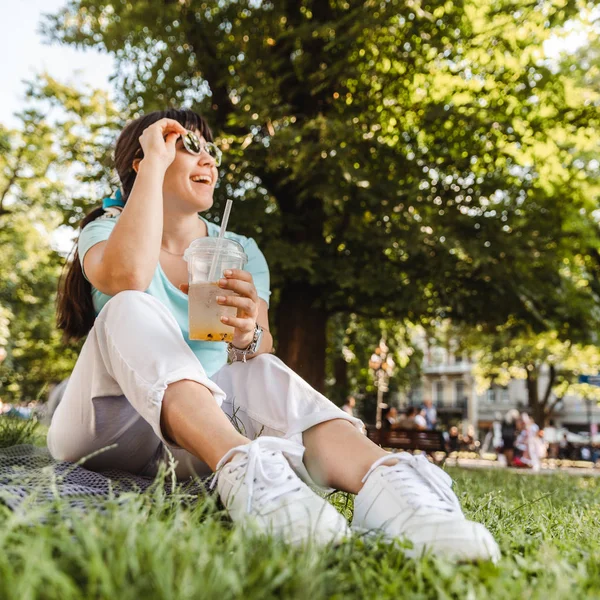 woman holding cool drink in city park. blurred background. wide angel