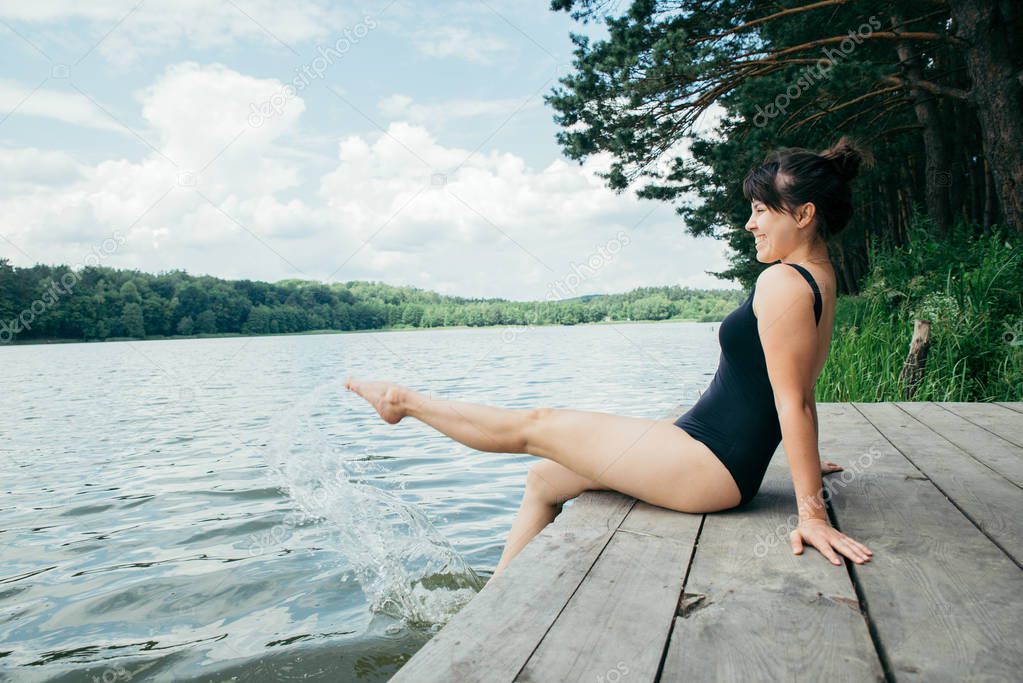 young pretty woman sitting on wooden dock legs in water
