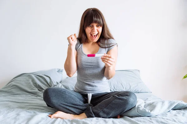 Молода Щаслива Жінка Сидить Ліжку Дивлячись Позитивний Тест Вагітність — стокове фото
