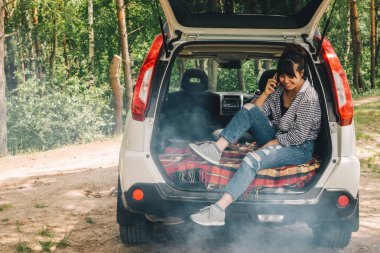 Barbekü yanıyor. araba bagajında oturan kadın. araba seyahat kavramı