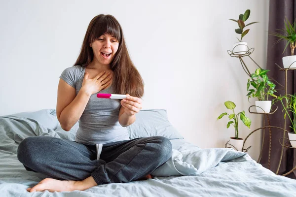 Unga Lyckliga Kvinnan Sitter Sängen Tittar Positivt Graviditetstest — Stockfoto