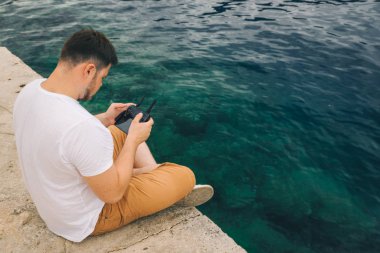 deniz su kenarında oturan dron denetleyicisi olan adam. kopya alanı