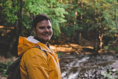 Adam sarı yağmurluk ormanın ortasında dur. Hiking kavramı