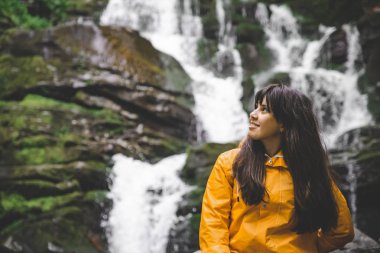 şelale zemin üzerine sarı yağmurluk gülümseyen kadın. Hiking kavramı