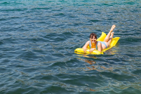 青い海の水で黄色のマットレスの上の若い大人の女性 夏の時間概念 — ストック写真