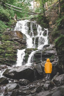 sarı yağmurluk ayakta ve şelale arayan bir kadın. Hiking kavramı