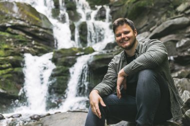 arka plan üzerinde şelale ile kayaya oturan adam. seyahat kavramı