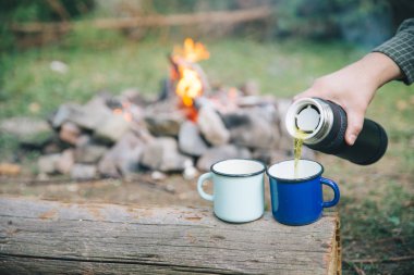 El metal bardak çay dökün. arka plan üzerinde kamp ateşi. Hiking kavramı