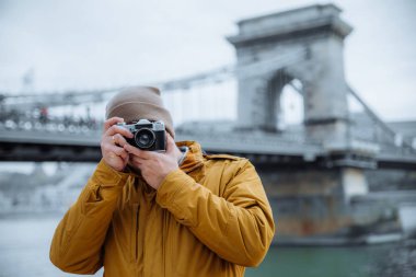Genç adam nefret ediyorum eski retro kamera fotoğraf çekimi. arka plan üzerinde eski zincir köprü