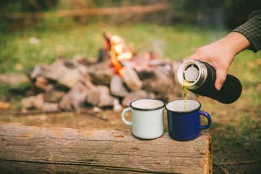 El metal bardak çay dökün. arka plan üzerinde kamp ateşi. Hiking kavramı