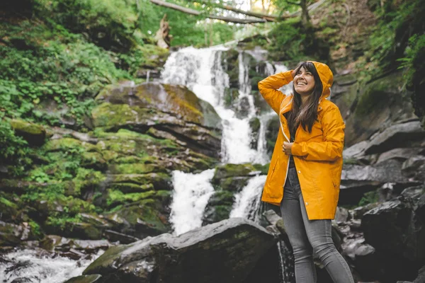 sarı yağmurluk ayakta ve şelale arayan bir kadın. Hiking kavramı