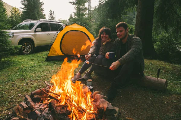 couple sitting near camp fire and drinking tea and telling stories . tent and suv on background. union with nature