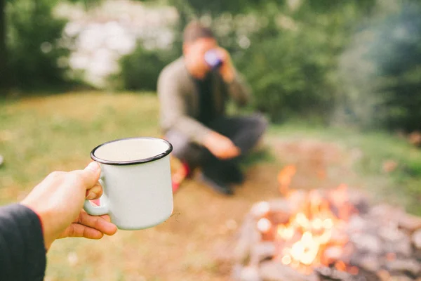 woman hold cup. first point of view. man eating and drinking near fire. camping concept