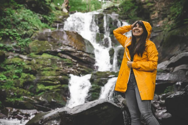 sarı yağmurluk ayakta ve şelale arayan bir kadın. Hiking kavramı