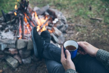 ilk bakış. kamp ateşi yakınındaki metal fincan çay içme adam. Hiking