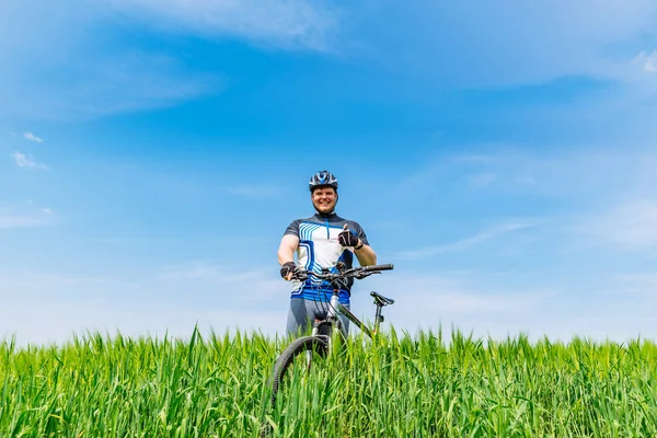 若い大人の笑みを浮かべての男は背景に青い空の下に緑の大麦に自転車に立って コピー スペース — ストック写真