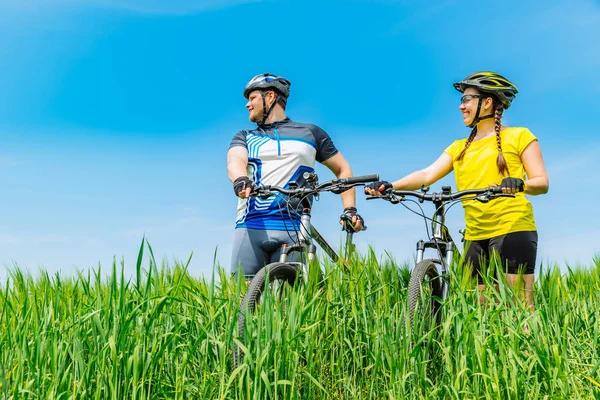 若い強者と自転車で緑の草原に立っている女性の笑顔します ライフ スタイル — ストック写真