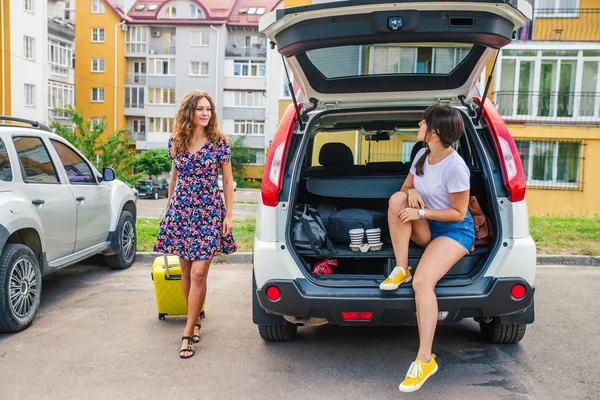 two woman packing luggage in car trunk. road trip