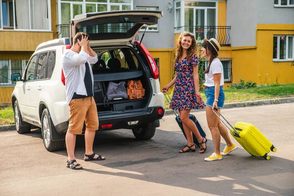 one man and two women loading bags in car trunk. road trip