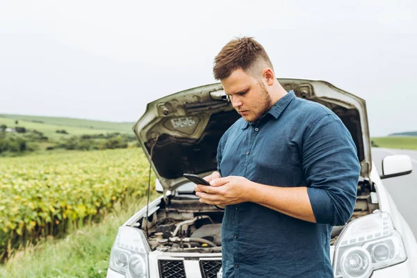 adam telefonu ile kırık araba önünde dur. hiçbir yerin ortasında kırık