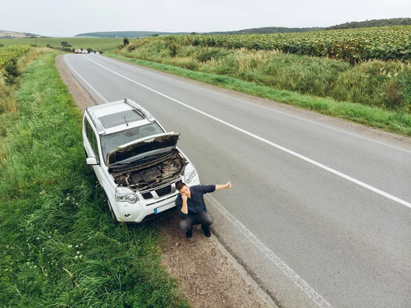 壊れた車の近くの道路に座っている男 助けをしようとして停止車 道端で壊れた車 — ストック写真