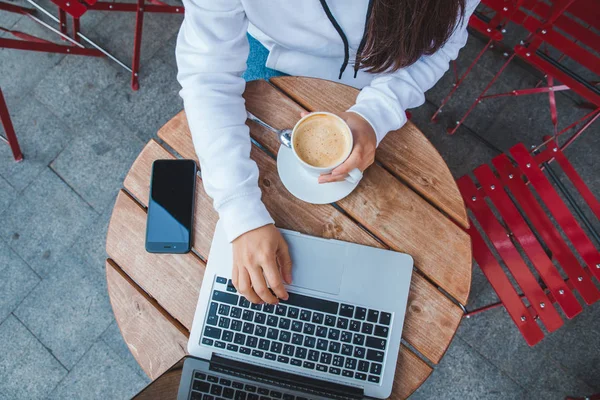 在城市咖啡馆的笔记本电脑上工作的女人拿着杯咖啡 — 图库照片