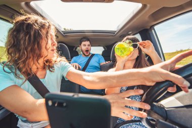 bir grup insan arabada. kadını sürücüsü içme su ve yolda bakma. güvenli sürüş