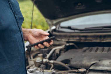 telefon elinde dostum. arka plan açılan kaputa. kırık araba