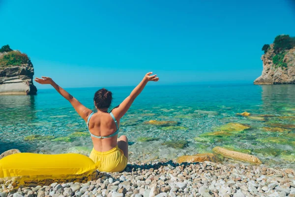 坐在海边的女人举手 黄色充气床垫 — 图库照片