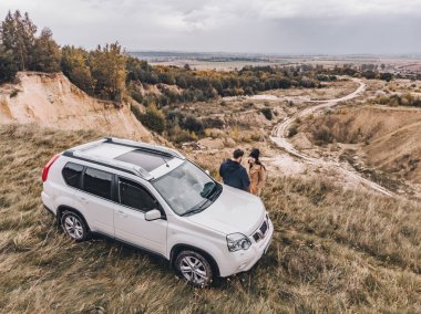üstten güzel görünüm uçurumun altındaki suv arabaya yakın çift ayakta. bulutlu sonbahar hava