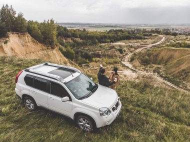 üstten güzel görünüm uçurumun altındaki suv arabaya yakın çift ayakta. bulutlu sonbahar hava