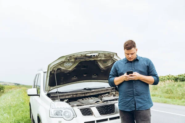 man stand in front of broken car with phone. broken in the middle of nowhere