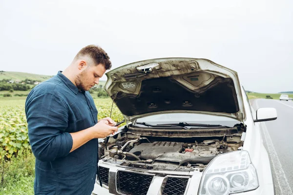 man stand in front of broken car with phone. broken in the middle of nowhere