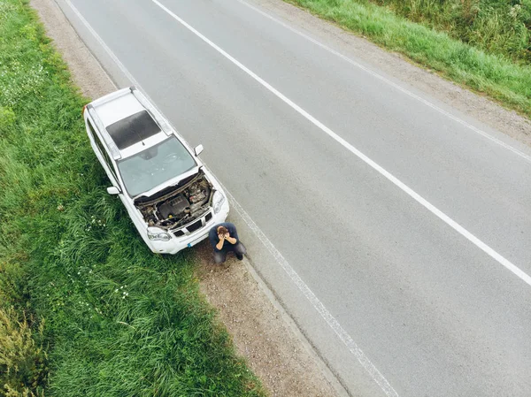 Mann sitzt auf Straße neben kaputtem Auto Versuch, Auto anzuhalten und Hilfe zu holen — Stockfoto