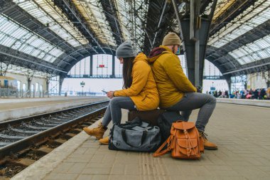 sıkılmış çift onların çantalar için tren bekleyen oturmak. telefonları beklerken kontrol
