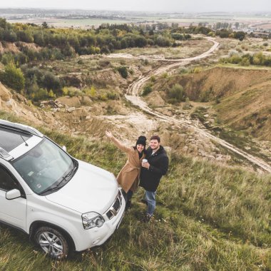 üstten güzel görünüm uçurumun altındaki suv arabaya yakın çift ayakta. bulutlu sonbahar hava