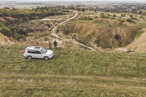 stock image couple standing on cliff in overcast weather near white suv car