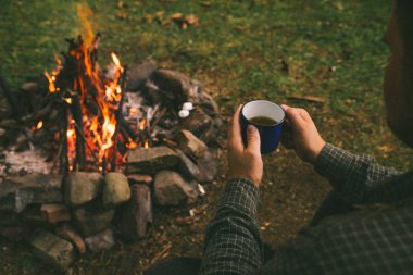 ilk bakış. kamp ateşi yakınındaki metal fincan çay içme adam. Hiking