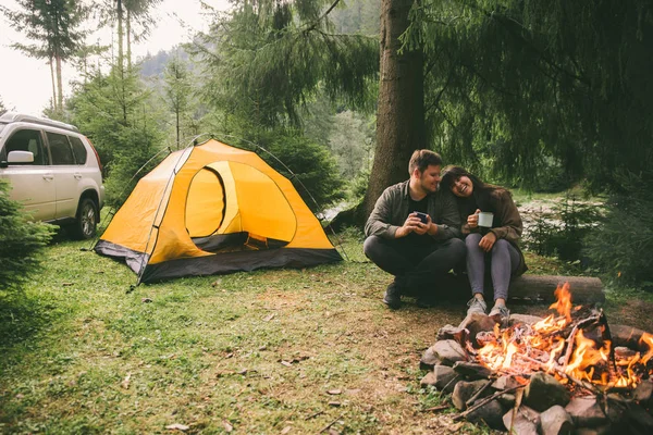 火と熱いお茶を飲むのそばに座ってカップル ハイキングのコンセプトです 背景のテントが付いている車 — ストック写真