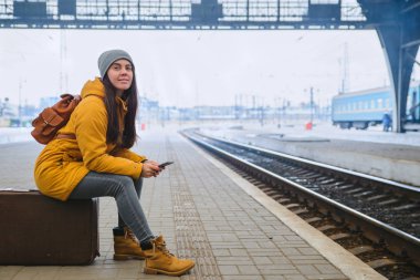Tren Tren İstasyonu için kadın bekleyin. seyahat kavramı. zaman öldürmek için telefona internet sörf